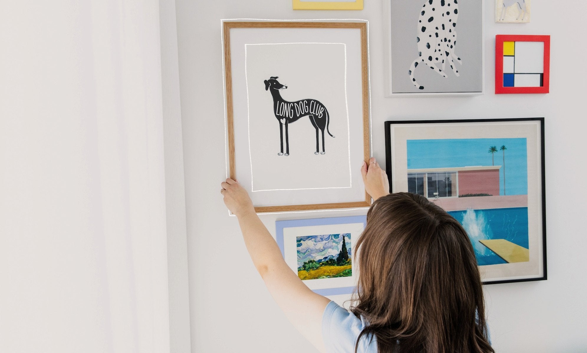 Woman standing at gallery wall, hanging a greyhound print from Long Dog Club