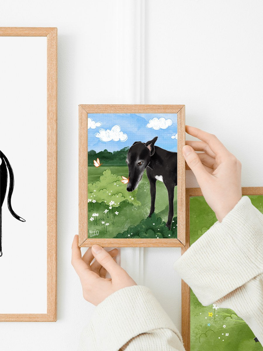 Woman is hanging a greyhound illustration print on a gallery wall of dog art