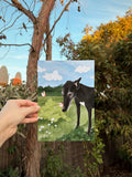 Bespoke print of a greyhound in the garden is being held up outside in front of native foliage