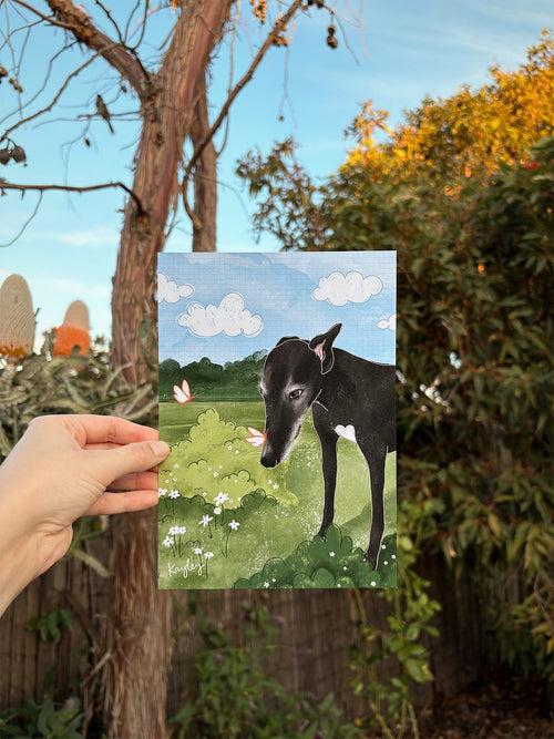 Bespoke print of a greyhound in the garden is being held up outside in front of native foliage