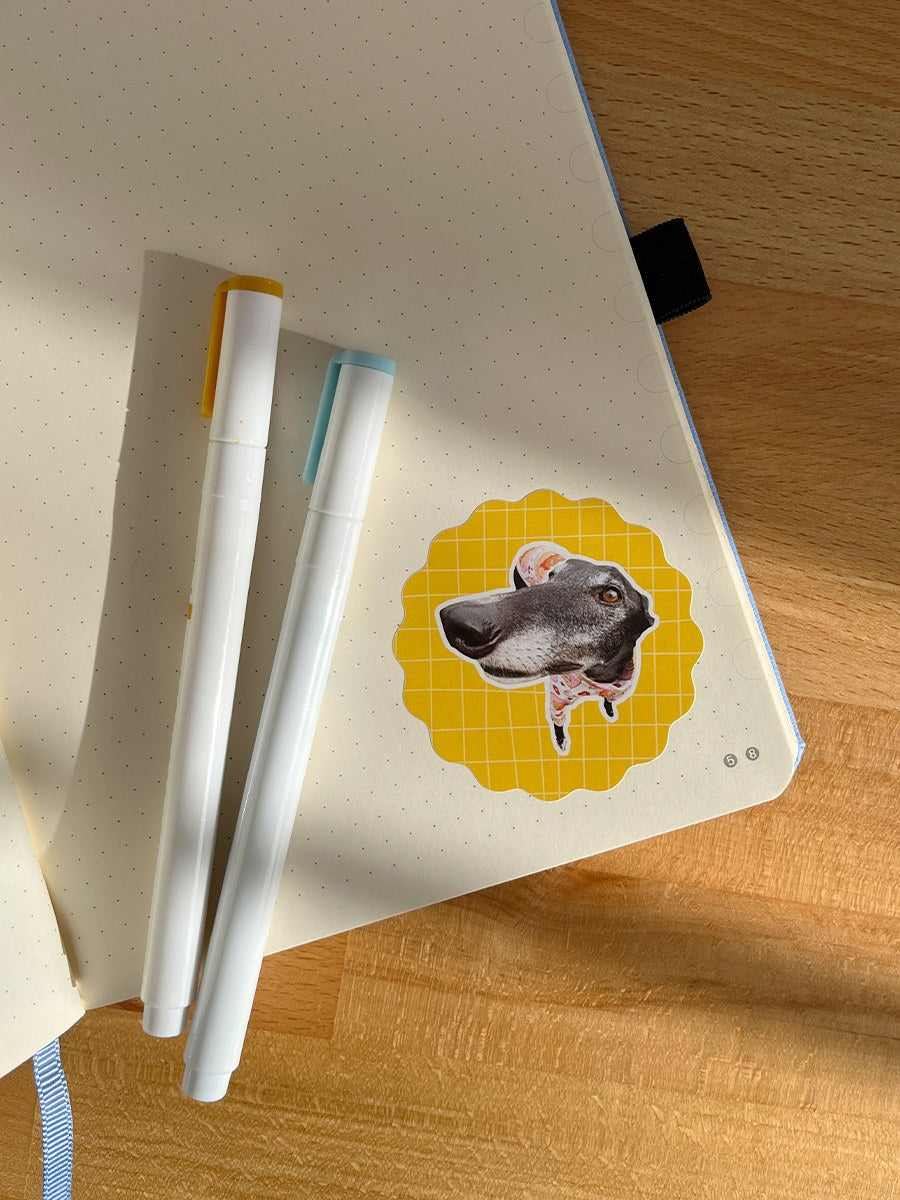 Notebook with a greyhound sticker next to some pens on a wooden table. 