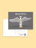 Front and back of the Saint Grey postcard by Elliott Fox on a pale yellow background. The front has a gray panel with the text 'Saint Grey' above a white winged statue with a gold heart detail.