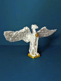 A white winged dog statue with outstretched wings and a gold base, photographed against a dark navy background. The hero artwork from the Saint Grey art exhibition by Elliott Fox. 