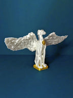 A white winged dog statue with outstretched wings and a gold base, photographed against a dark navy background. The hero artwork from the Saint Grey art exhibition by Elliott Fox. 