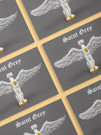 A pack of official Saint Grey exhibition postcards by Elliott Fox. The artwork is grey and features a greyhound statue with wings and a gold heart.