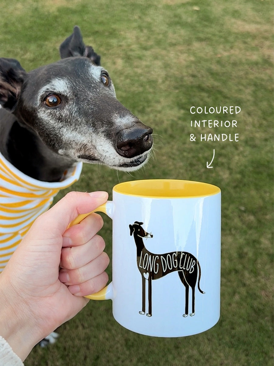 Chilli, a black greyhound, sniffs the sighthound mug from Long Dog Club