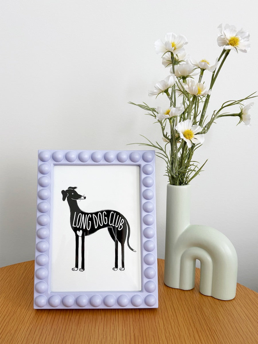 A5 greyhound print sitting in a lilac frame on a table next to flowers