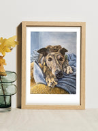 A framed art print of a brindle greyhound called Hannah gazing at the camera, beside a vase with flowers in it. The original portrait was painted by Elliott Fox.