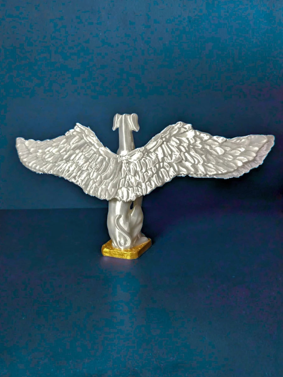 A winged greyhound miniature statue with outstretched wings, as depicted from behind. There is gold detailing on the bottom of the figure. Titled "Saint Grey" by Elliott Fox.