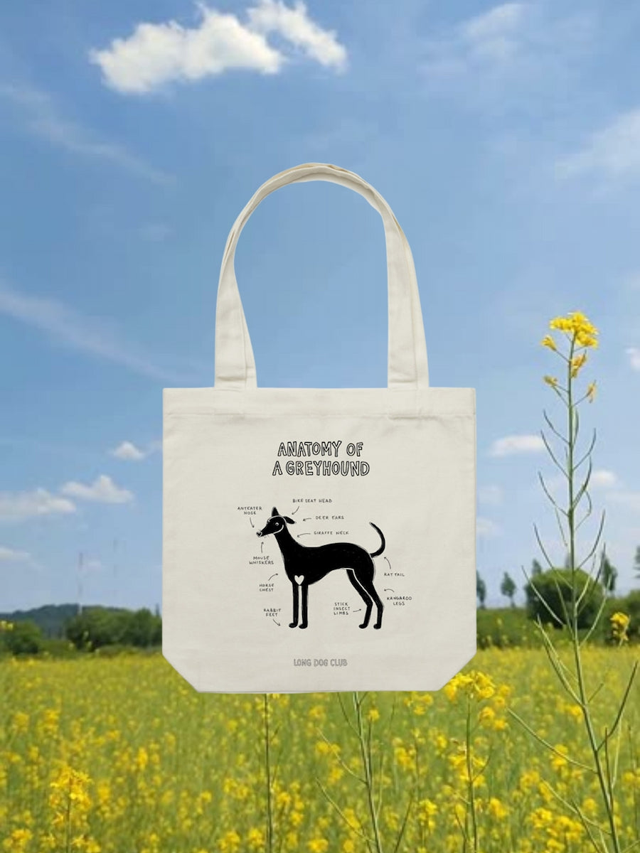 Tote bag with a dog illustration and text in a field with yellow flowers and blue sky.
